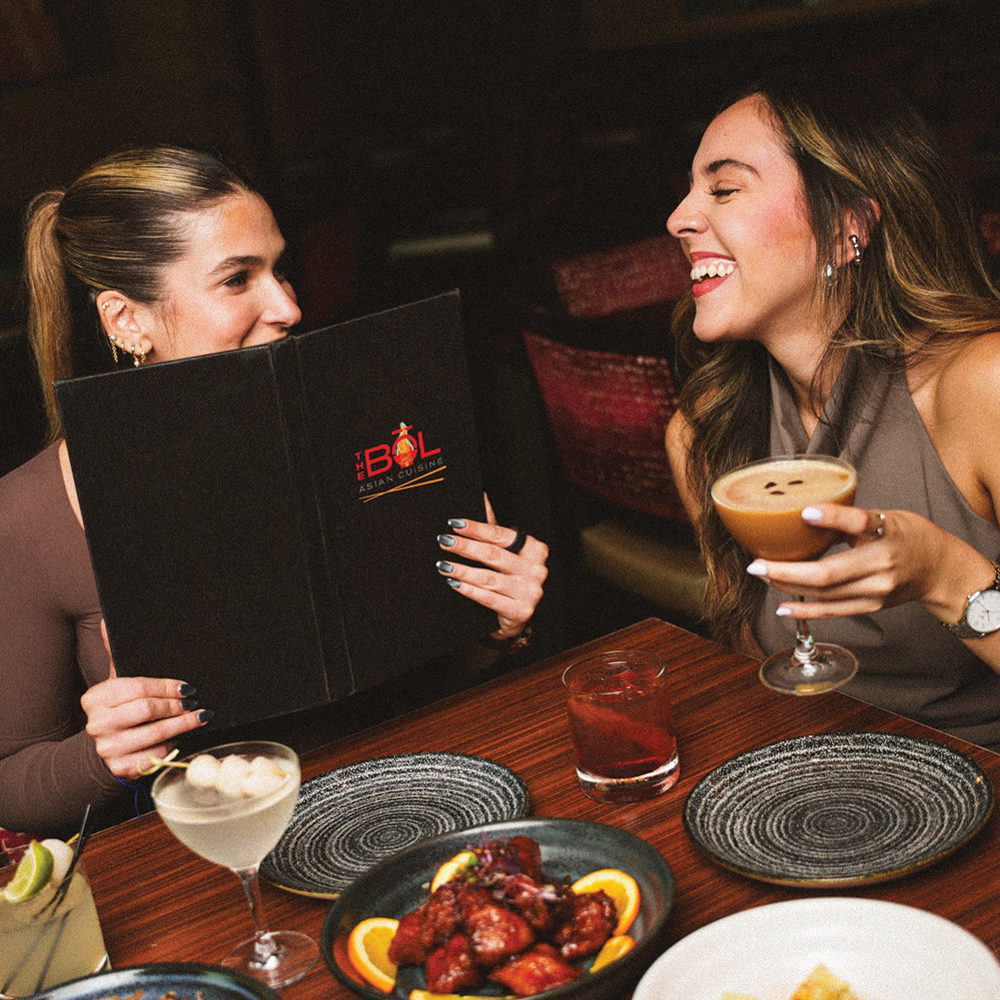 two women smiling with drinks and a menu