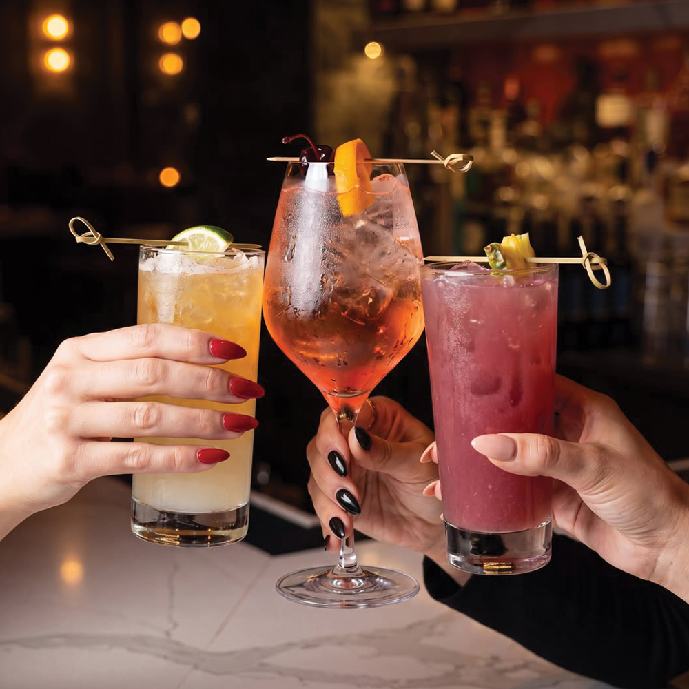 three hands holding drinks touching glasses together