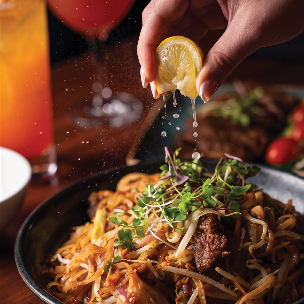 a hand squeezing lemon over a plat of food